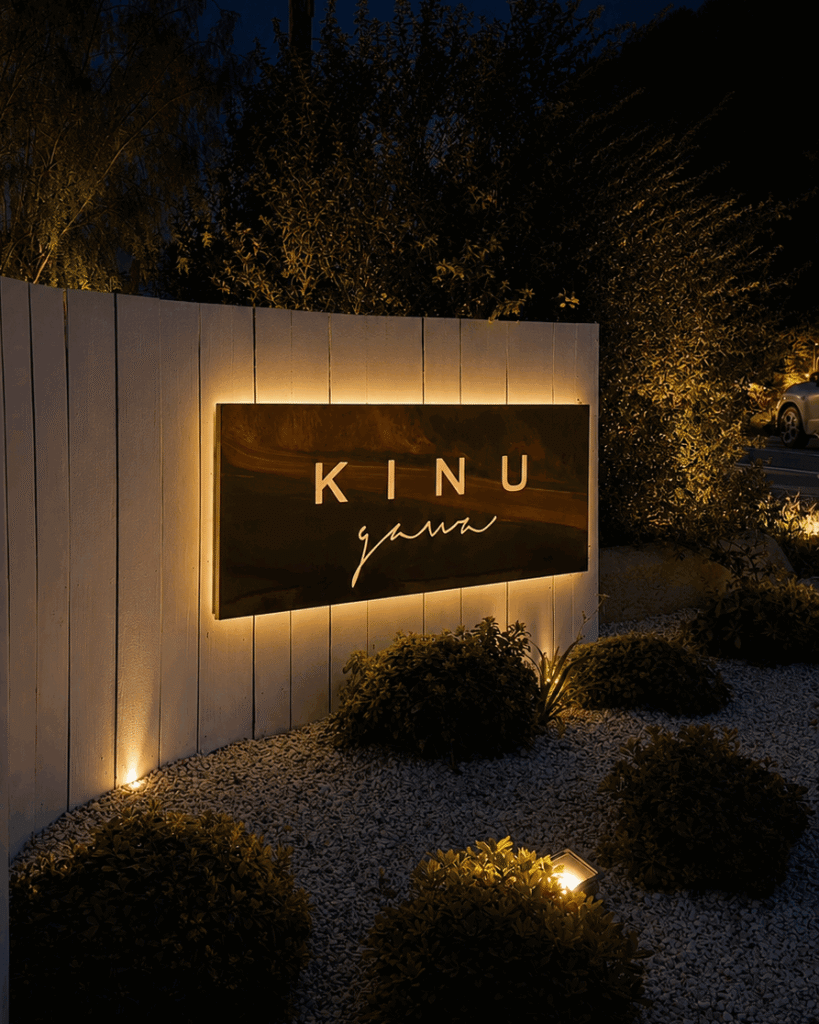 Kinugawa Ramatuelle restaurant entrance at night with an illuminated sign, white fence, landscaped garden, and warm ambient lighting in Saint-Tropez, France.