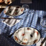 Le Club 55 signature seashell-pattern tableware on blue linen, Saint-Tropez