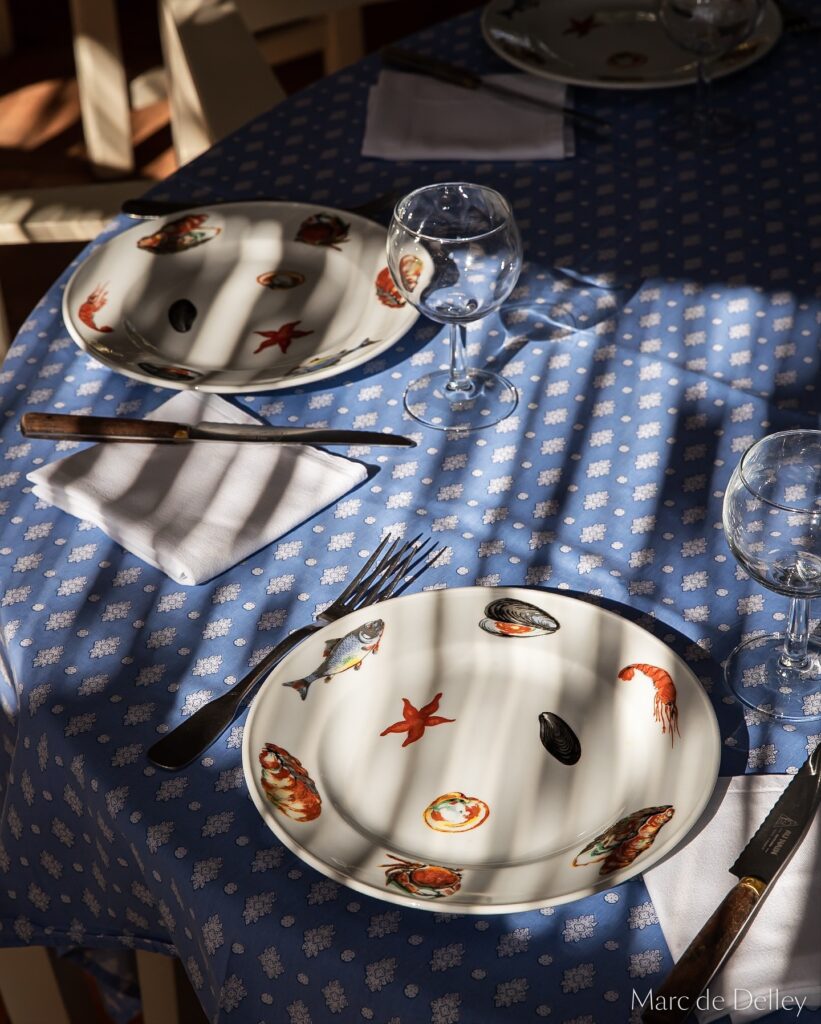Le Club 55 signature seashell-pattern tableware on blue linen, Saint-Tropez