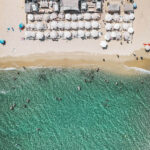 Aerial view of Verde Beach with rows of white parasols along the sand and turquoise water
