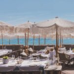 Verde Beach restaurant tables dressed in white linen under fringed parasols facing the sea