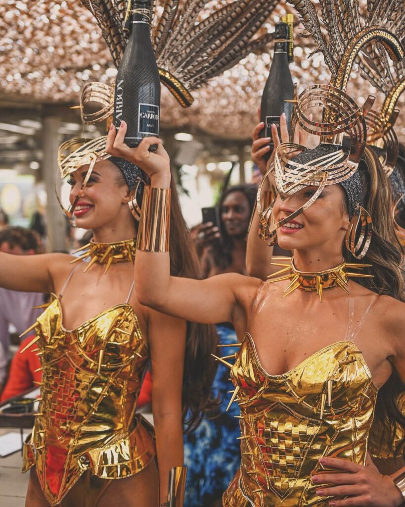 Costumed performers carrying champagne bottles during a parade at Verde Beach