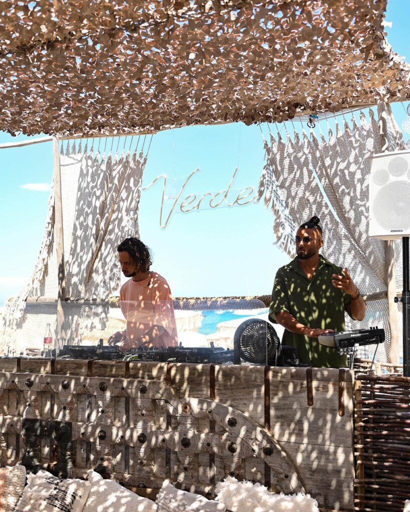 DJs performing at the Verde Beach booth beneath the illuminated Verde sign