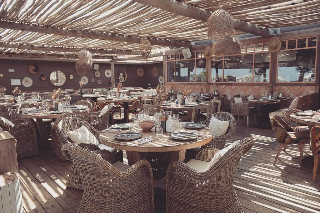 Verde Beach restaurant interior with woven armchairs, wooden decking and a thatched ceiling