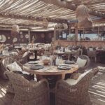 Verde Beach restaurant interior with woven armchairs, wooden decking and a thatched ceiling