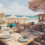 Beachfront table set for lunch at Verde Beach with fringed parasols and yachts on the water