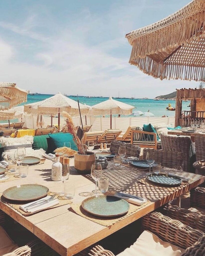 Beachfront table set for lunch at Verde Beach with fringed parasols and yachts on the water