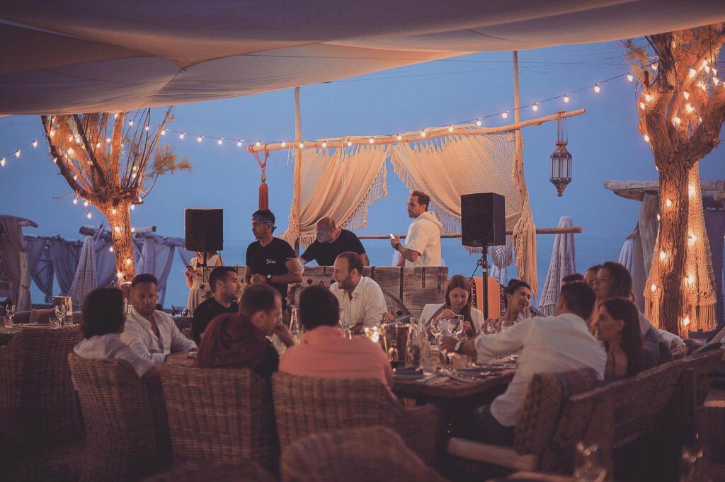 Guests dining at dusk under festoon lights at Verde Beach, with a live music setup and the sea behind