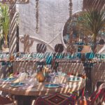 Boho table setting at Verde Beach with turquoise plates, wine glasses and woven chairs under a macrame backdrop