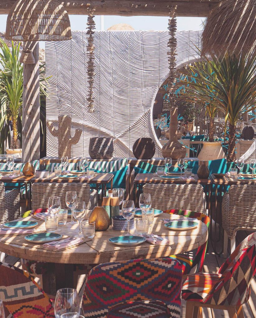 Boho table setting at Verde Beach with turquoise plates, wine glasses and woven chairs under a macrame backdrop