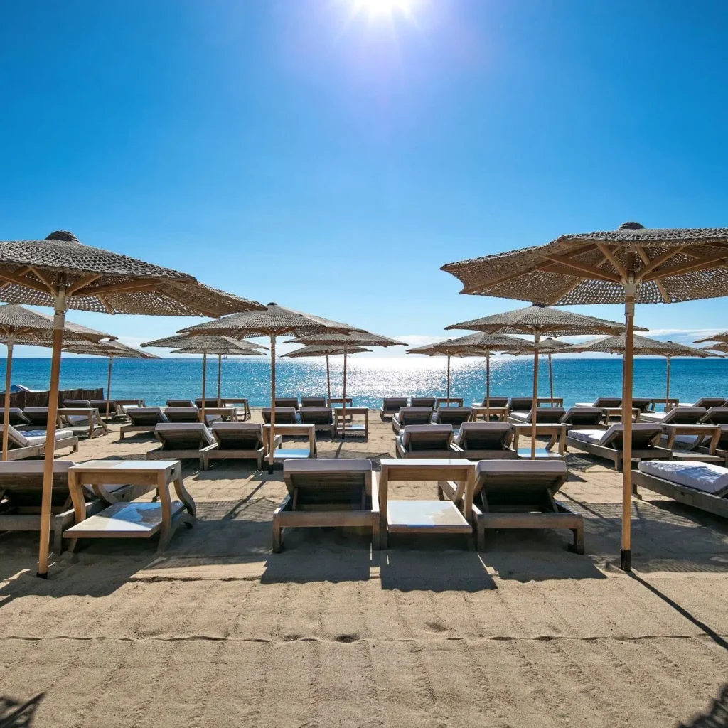 Sunbeds and straw umbrellas facing a sunlit sea at Byblos Beach Ramatuelle