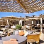 Cushioned daybed lounge area with boat-shaped seating on the sand at Byblos Beach Ramatuelle