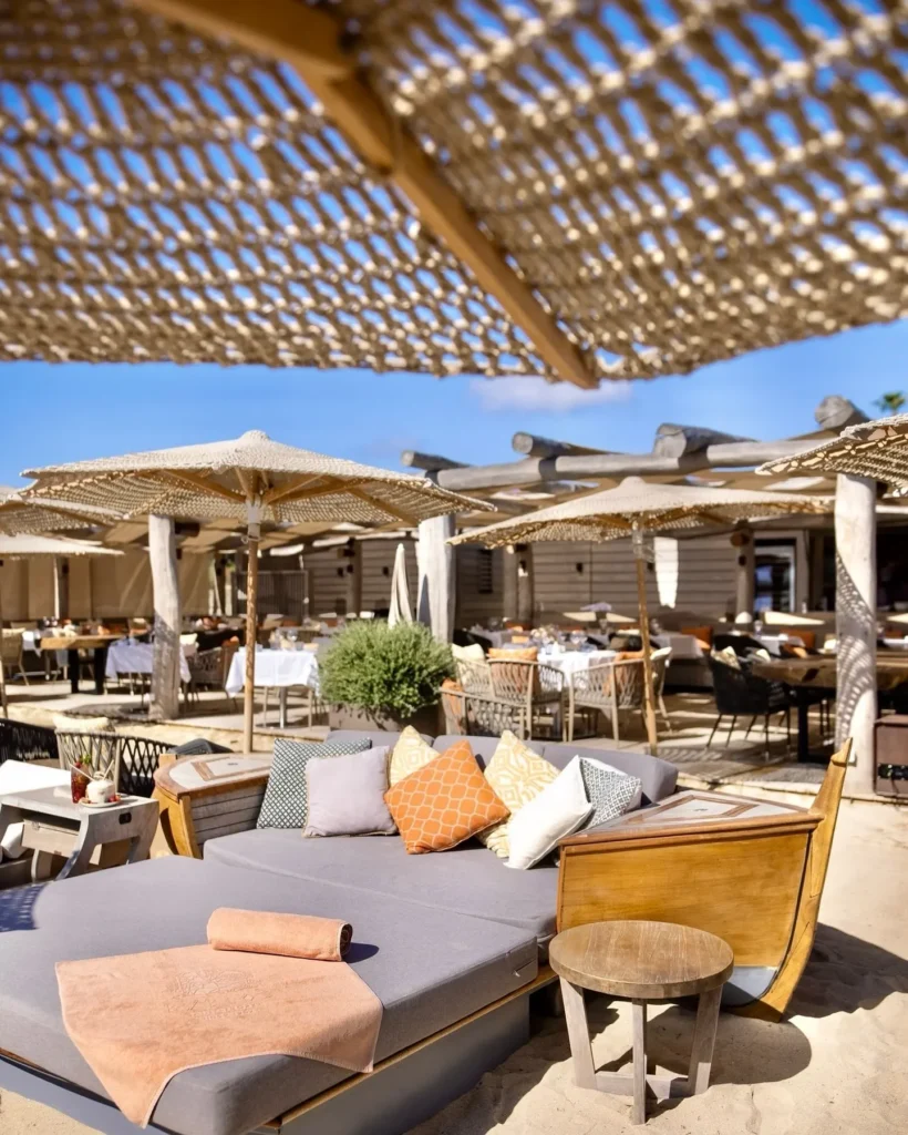 Cushioned daybed lounge area with boat-shaped seating on the sand at Byblos Beach Ramatuelle