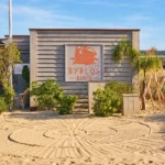 Byblos Beach signage on a weathered wooden beach hut with raked sand at Byblos Beach Ramatuelle