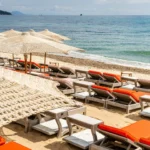 Sunbeds with orange cushions and straw umbrellas beside the sea at Byblos Beach Ramatuelle