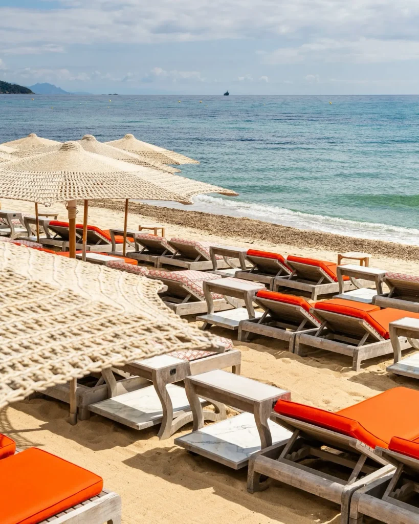Sunbeds with orange cushions and straw umbrellas beside the sea at Byblos Beach Ramatuelle