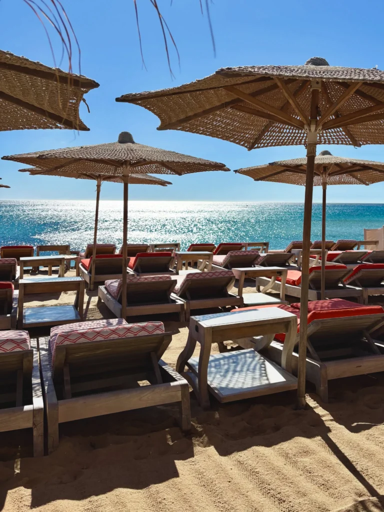 Sunbeds with red cushions under straw umbrellas beside the sea at Byblos Beach Ramatuelle