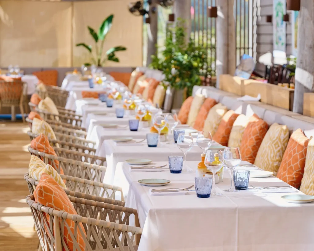 Long banquette lined with orange and yellow cushions beside set tables at Byblos Beach Ramatuelle