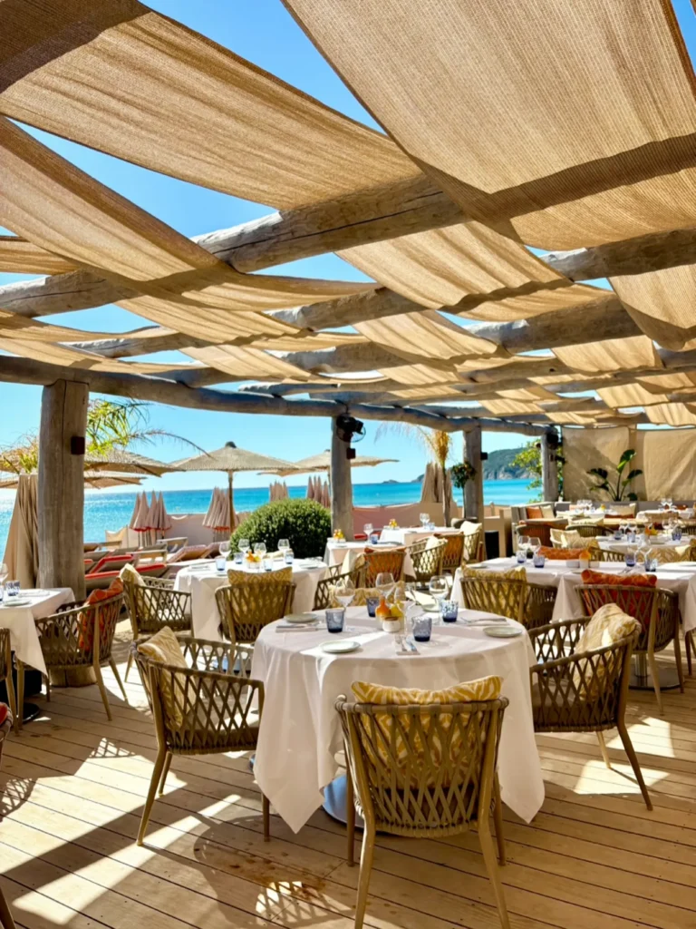 Round dining tables beneath a draped canopy with sea views at Byblos Beach Ramatuelle