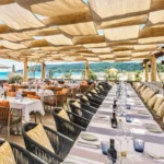 Long dining table and banquette seating under a canopy at Byblos Beach Ramatuelle