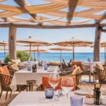 Oceanfront table setting with straw umbrellas and blue sea beyond at Byblos Beach Ramatuelle