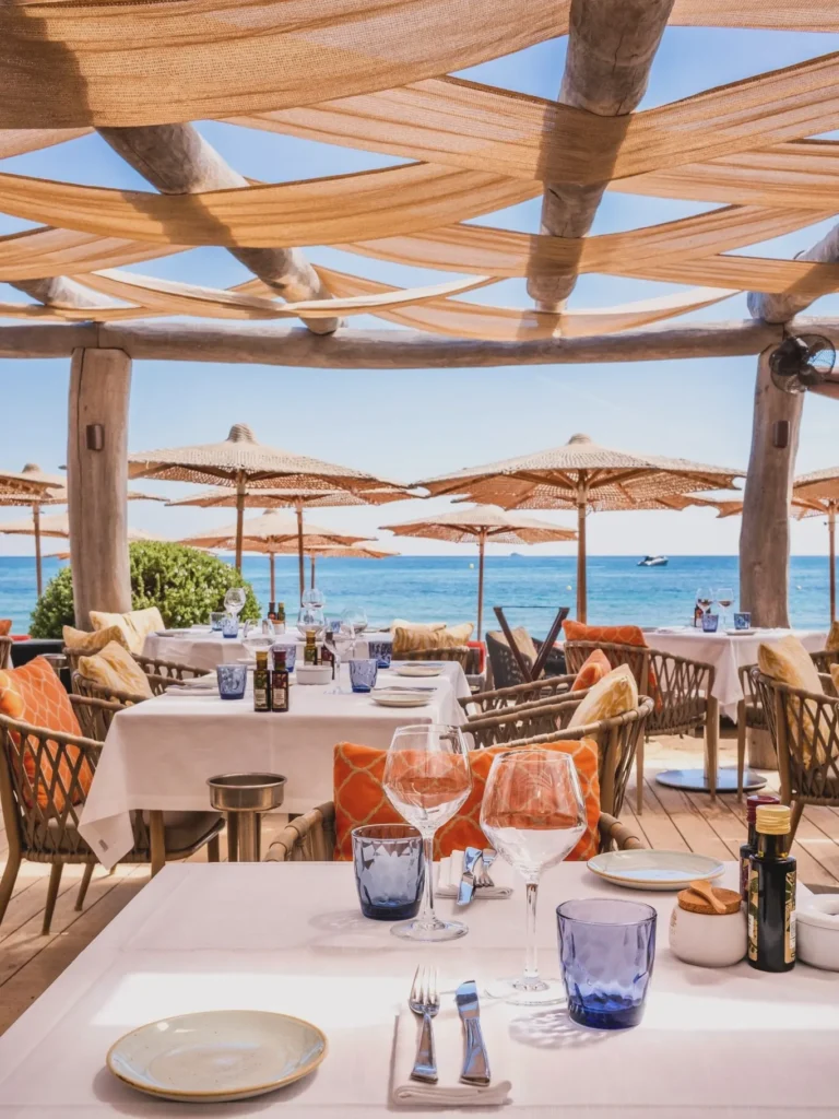 Oceanfront table setting with straw umbrellas and blue sea beyond at Byblos Beach Ramatuelle
