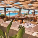 Restaurant tables framed by greenery with a bright sea view at Byblos Beach Ramatuelle