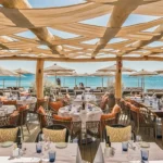 Beachfront restaurant terrace with rattan chairs and sea view at Byblos Beach Ramatuelle