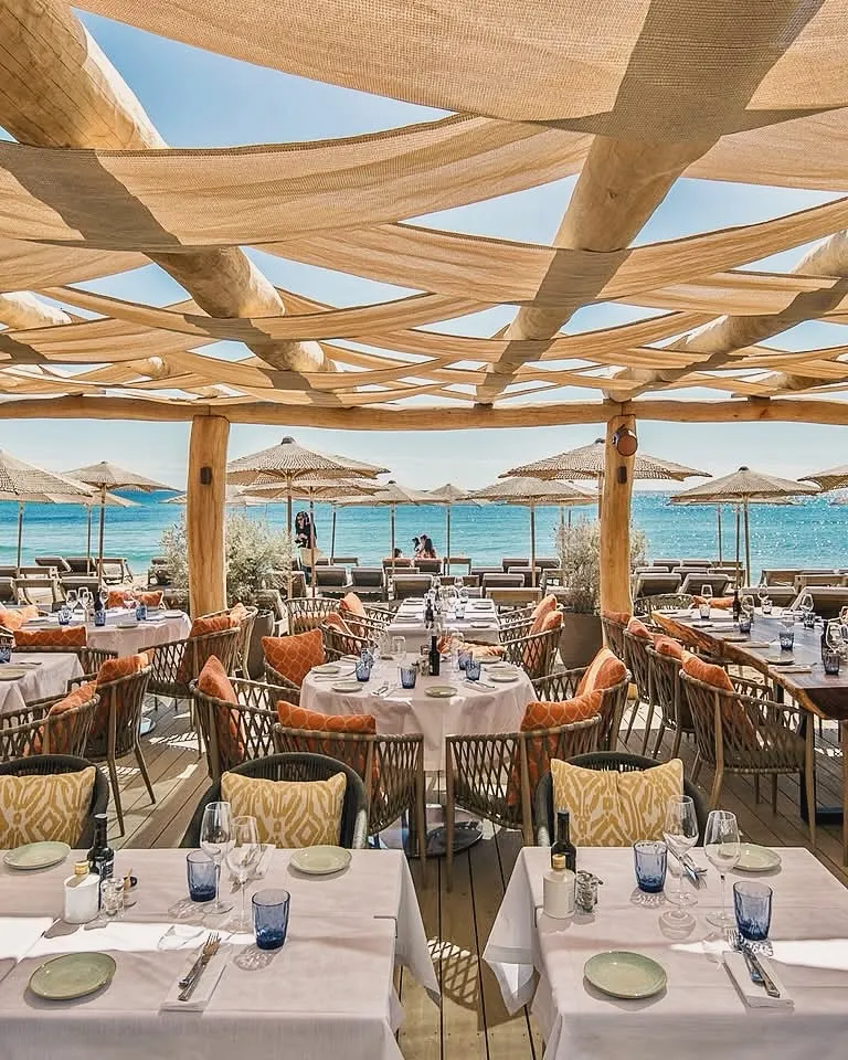 Beachfront restaurant terrace with rattan chairs and sea view at Byblos Beach Ramatuelle