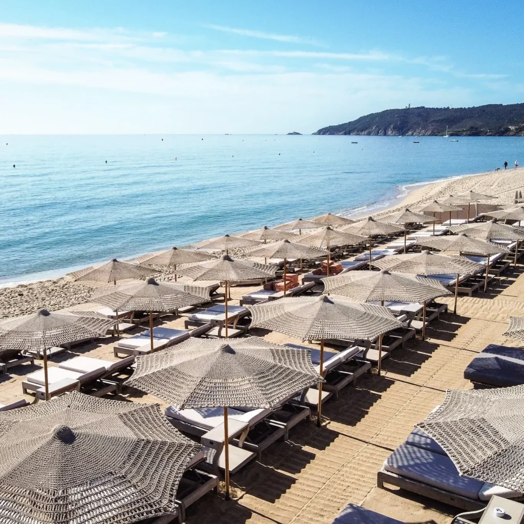 Aerial view of woven straw umbrellas and sunbeds lining the shore at Byblos Beach Ramatuelle