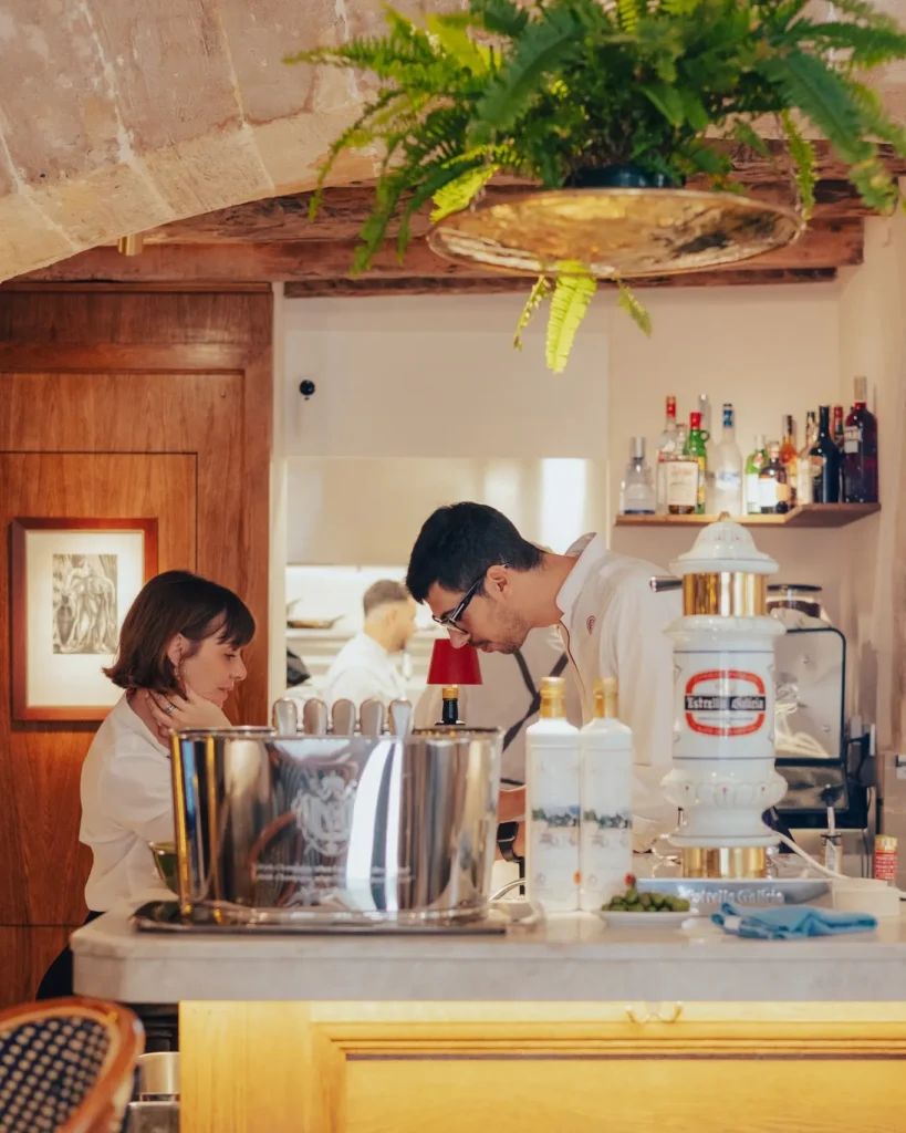 Staff working the counter with a beer tap beneath a hanging fern at El Caminito Palma