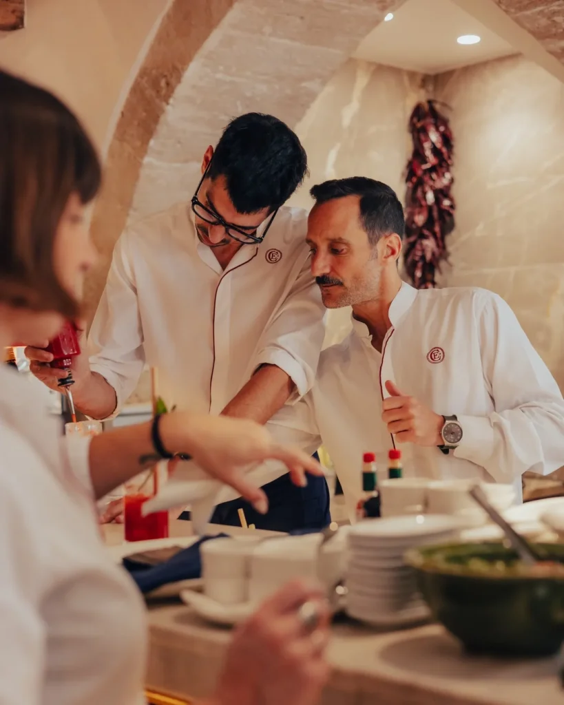 Two chefs conferring at the pass under a stone arch hung with dried peppers at El Caminito Palma