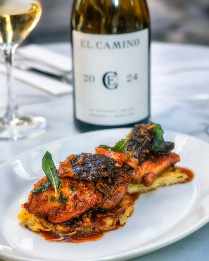 Glazed chicken topped with morels beside a bottle of house El Camino wine at El Caminito Palma