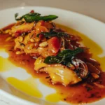 Chicken in a rich sauce with crispy sage and pine nuts on a white plate at El Caminito Palma