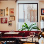Red banquette and set tables beneath framed vintage posters and a window at El Caminito Palma