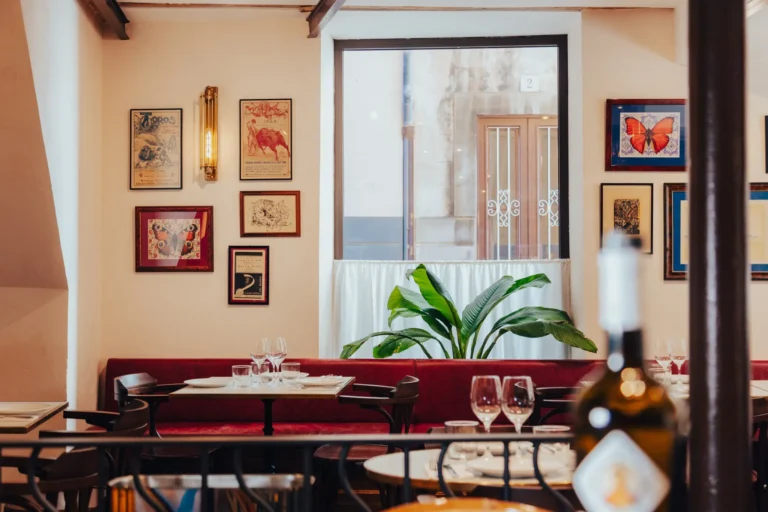 Red banquette and set tables beneath framed vintage posters and a window at El Caminito Palma