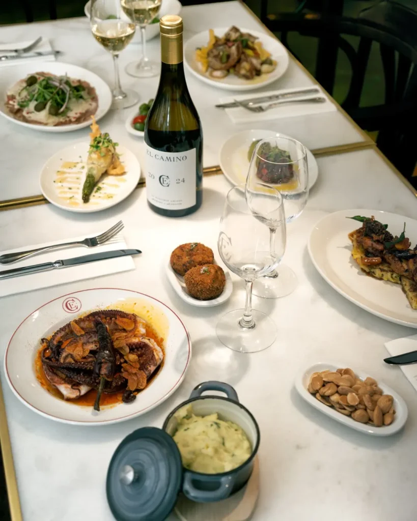Overhead spread of octopus, croquettes, almonds and house wine on a marble table at El Caminito Palma