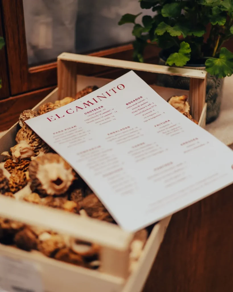 El Caminito menu resting on a crate of wild mushrooms beside a geranium at El Caminito Palma