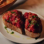 Toasted sourdough topped with grated tomato and parsley beside a loaf at El Caminito Palma