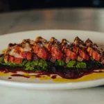 Sliced glazed pork over a herb pesto and jus on a white plate at El Caminito Palma