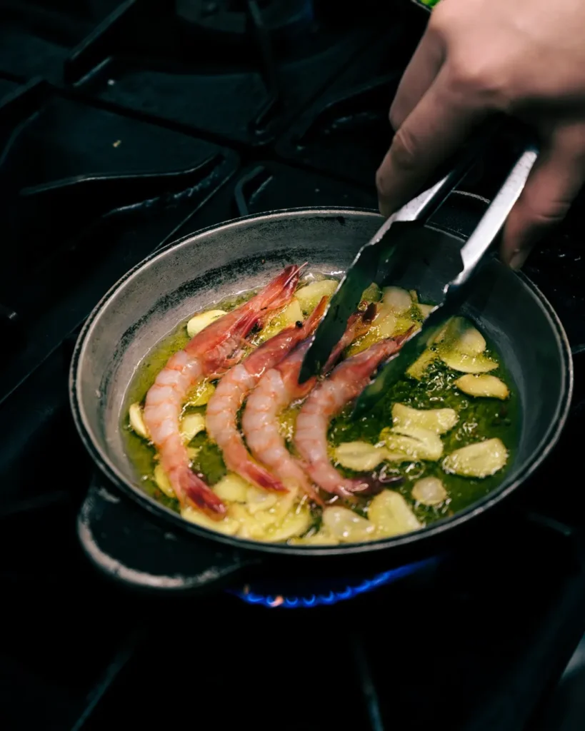 Prawns and sliced garlic sizzling in olive oil in a pan over a flame at El Caminito Palma