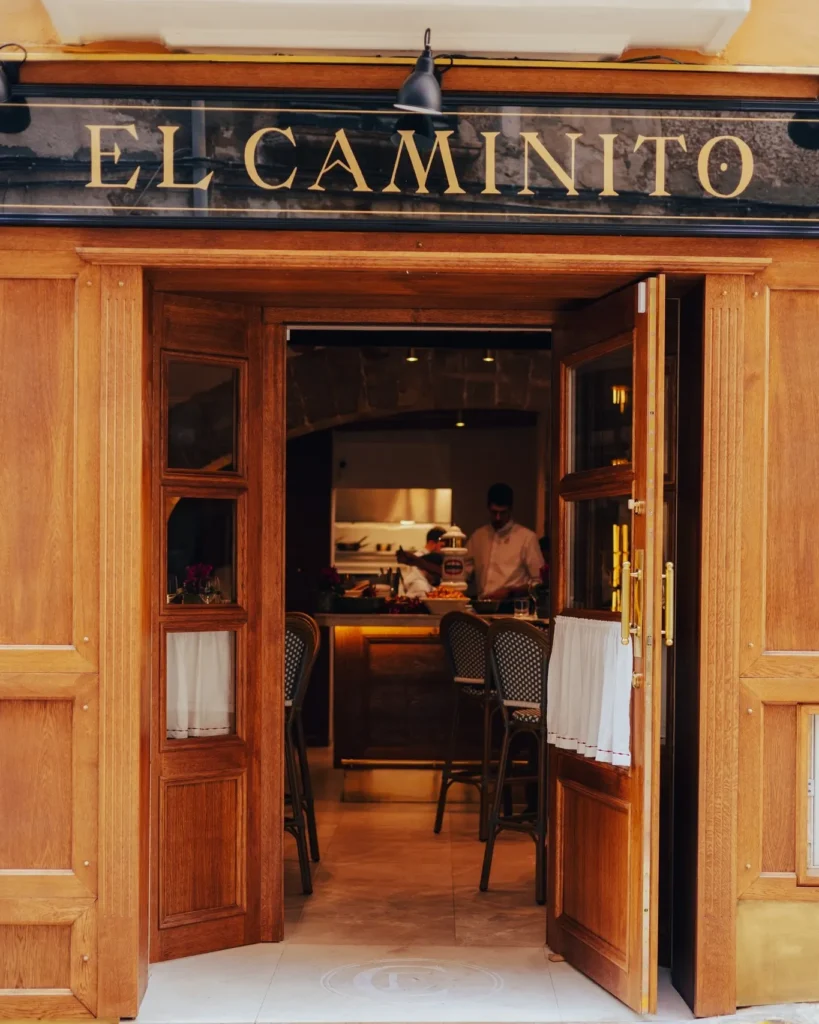 Gold El Caminito lettering above the wooden entrance doors opening to the kitchen at El Caminito Palma