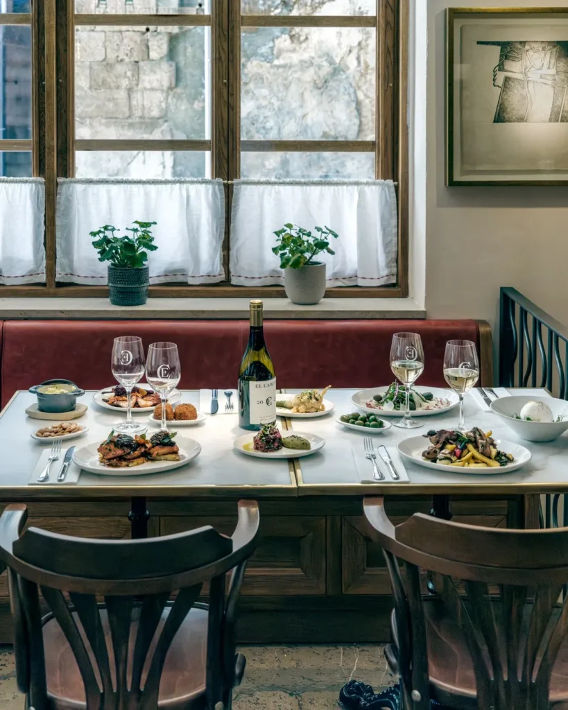 Banquette table laid with a full spread of dishes and wine by a curtained window at El Caminito Palma