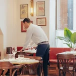 Waiter setting a banquette table beneath vintage posters at El Caminito Palma