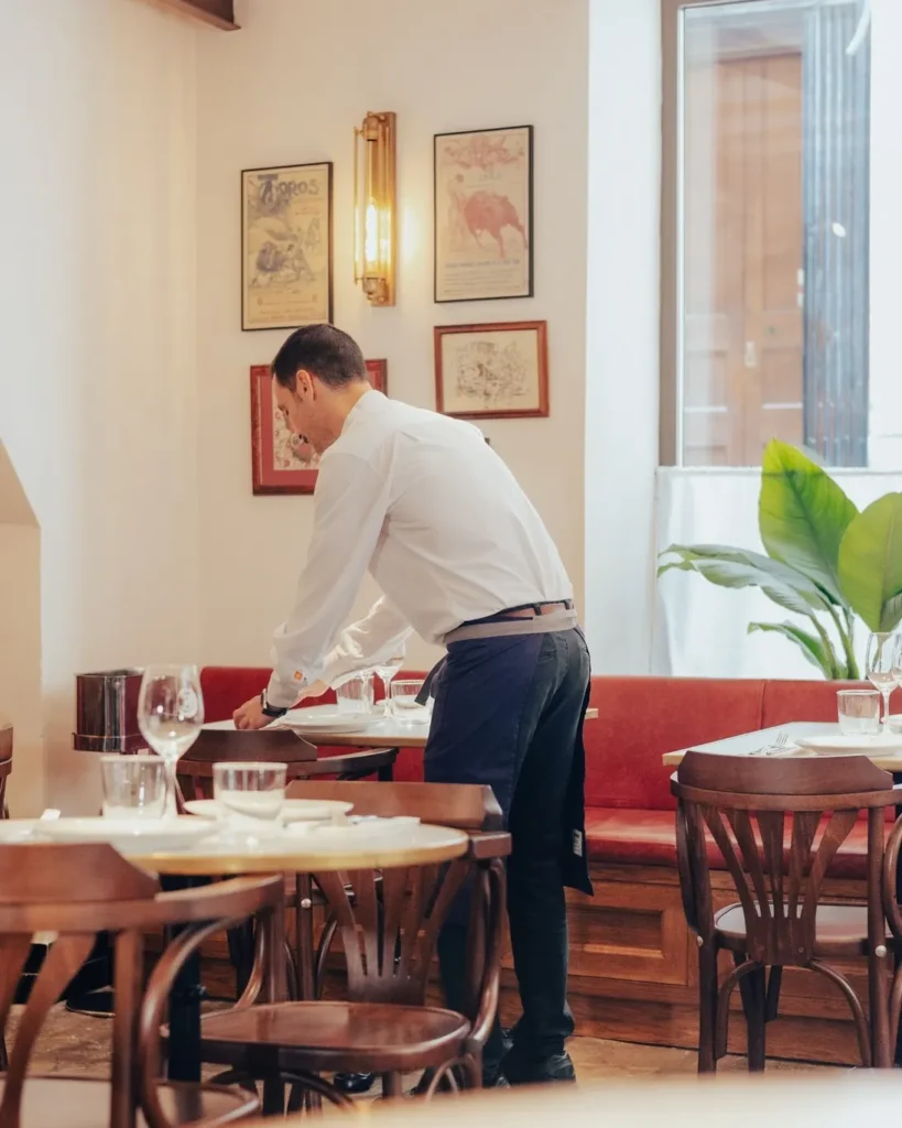 Waiter setting a banquette table beneath vintage posters at El Caminito Palma
