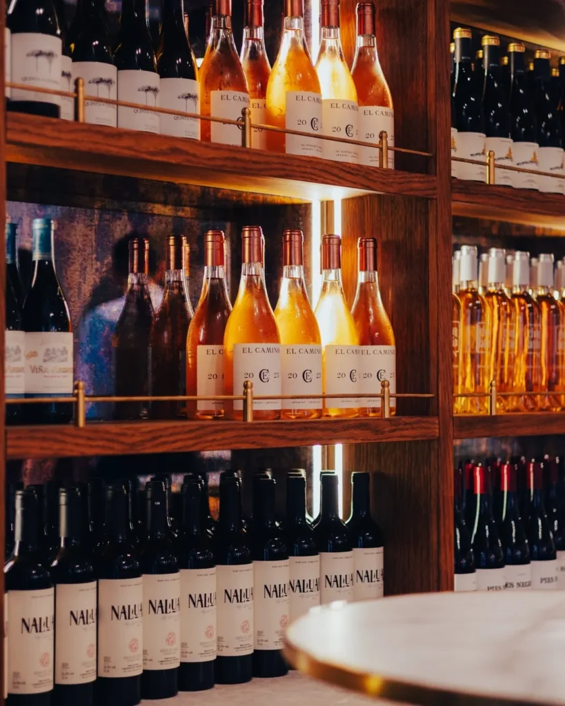 Backlit shelves lined with house El Camino and other wine bottles at El Caminito Palma