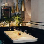 Marble banquette table with brass pendants, plants and a framed bull painting at El Camino Restaurant
