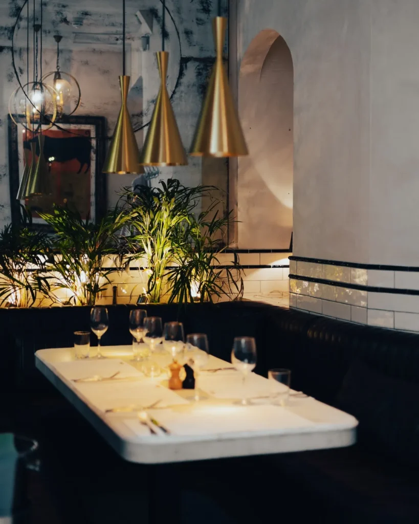 Marble banquette table with brass pendants, plants and a framed bull painting at El Camino Restaurant