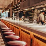 Marble counter with burgundy stools facing the open kitchen and brass pendant lights at El Camino Restaurant
