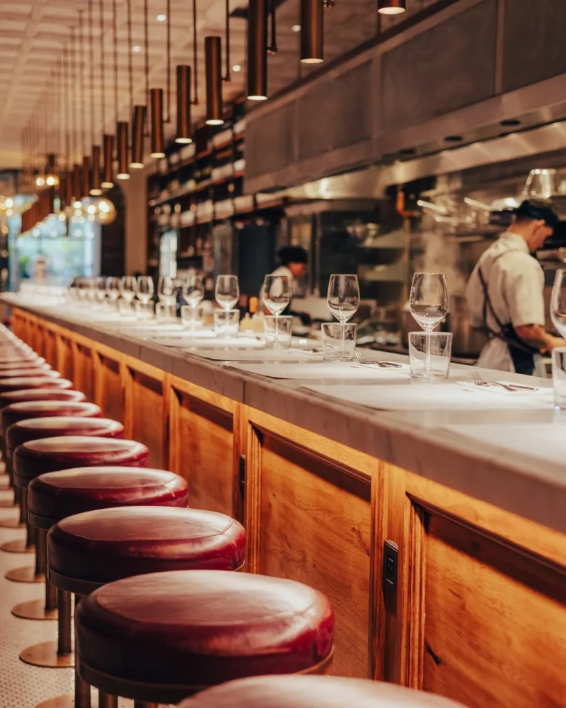 Marble counter with burgundy stools facing the open kitchen and brass pendant lights at El Camino Restaurant